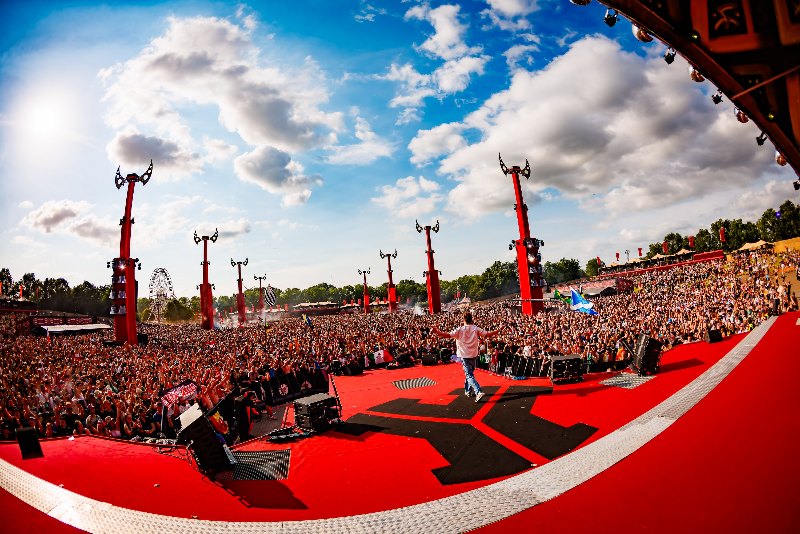 Fisheye view of a red stage platform with an MC and a huge daytime crowd under dramatic clouds