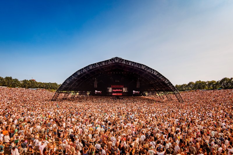 Huge arched festival stage under a blue sky with an enormous crowd stretching to the horizon