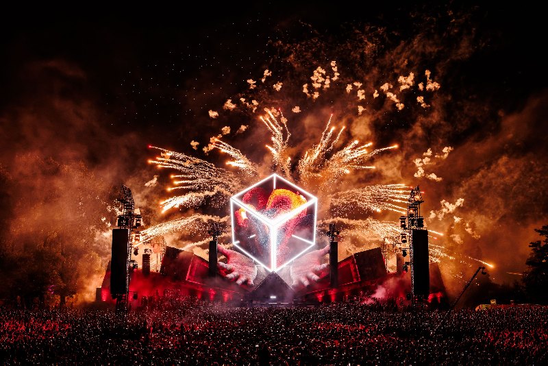 Glowing cube stage centrepiece with a large firework burst and a dense night-time crowd