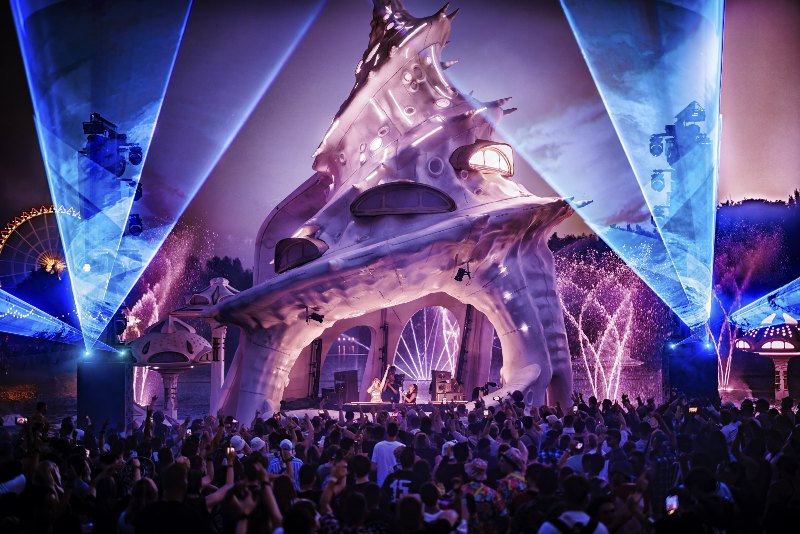 Mushroom-shaped stage design with blue laser beams above a dancing crowd