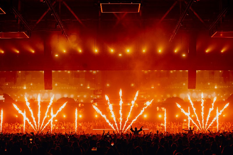 Rows of fire jets and warm orange light over a silhouetted arena crowd