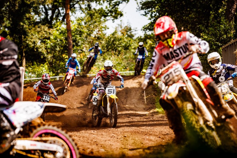 Motocross riders racing through a dusty forest track in a tight pack