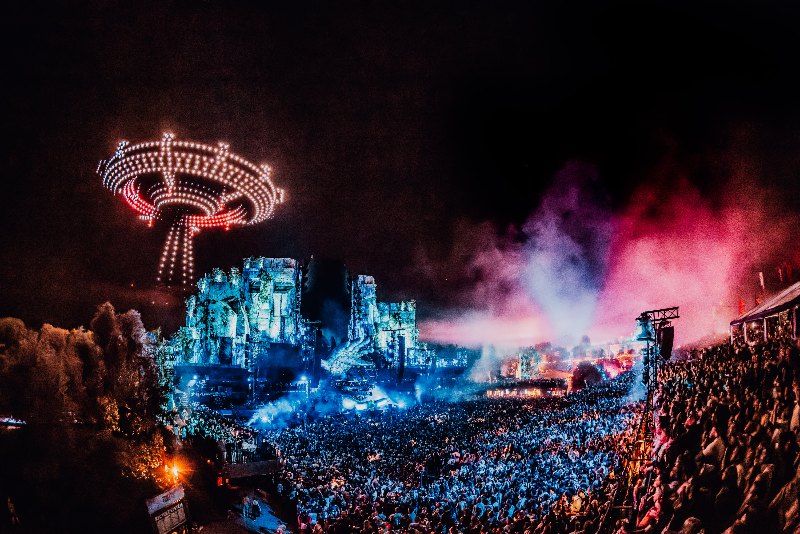 Drone show forming a glowing spinning-ride shape above a festival stage and a crowd at night