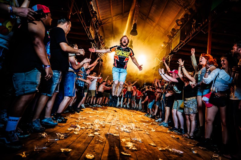 Performer leaping above reaching hands in a wooden barn stage lit by golden light at Zwarte Cross