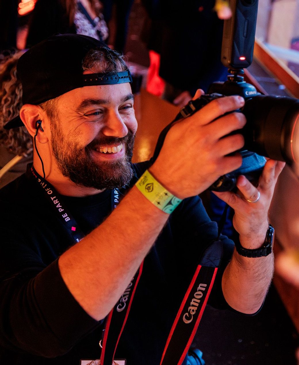 Martin Hols smiling behind his camera at an event, with an earpiece and a festival wristband