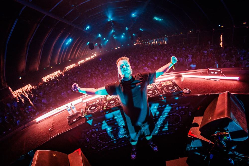 DJ with arms spread wide in his booth at Defqon.1, seen from above