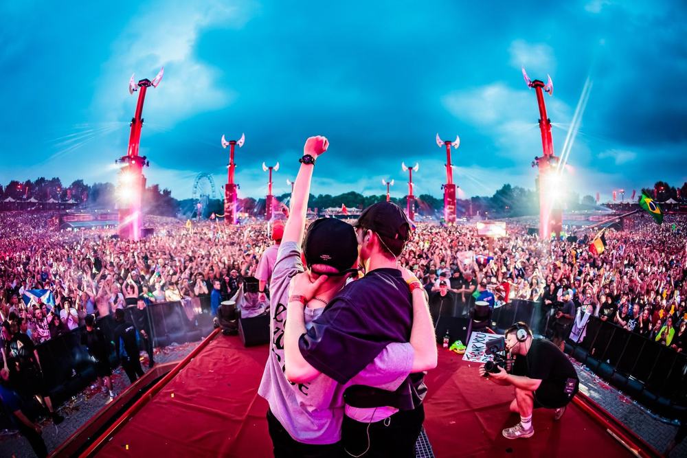 Two DJs embracing on a red stage at Defqon.1 in front of the crowd