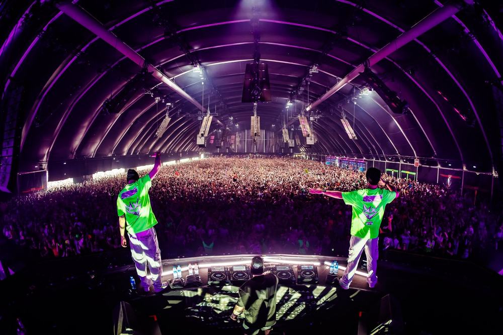 Two DJs in neon green outfits on stage in front of a packed Defqon.1 arena