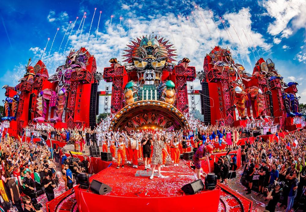 Defqon.1 main stage in daylight with a packed red-lit crowd area