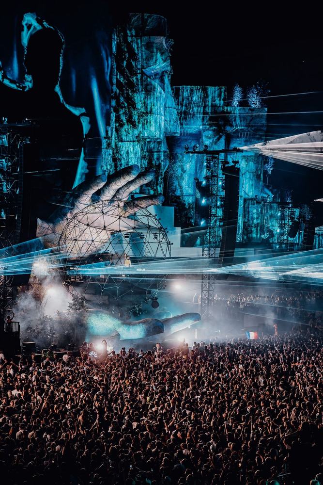 Mysteryland stage with a stone hand in blue light and a crowd below
