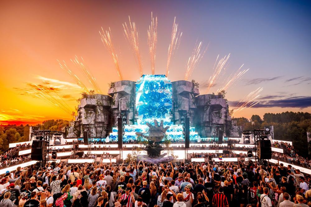Festival main stage at sunset with fireworks and a blue waterfall screen